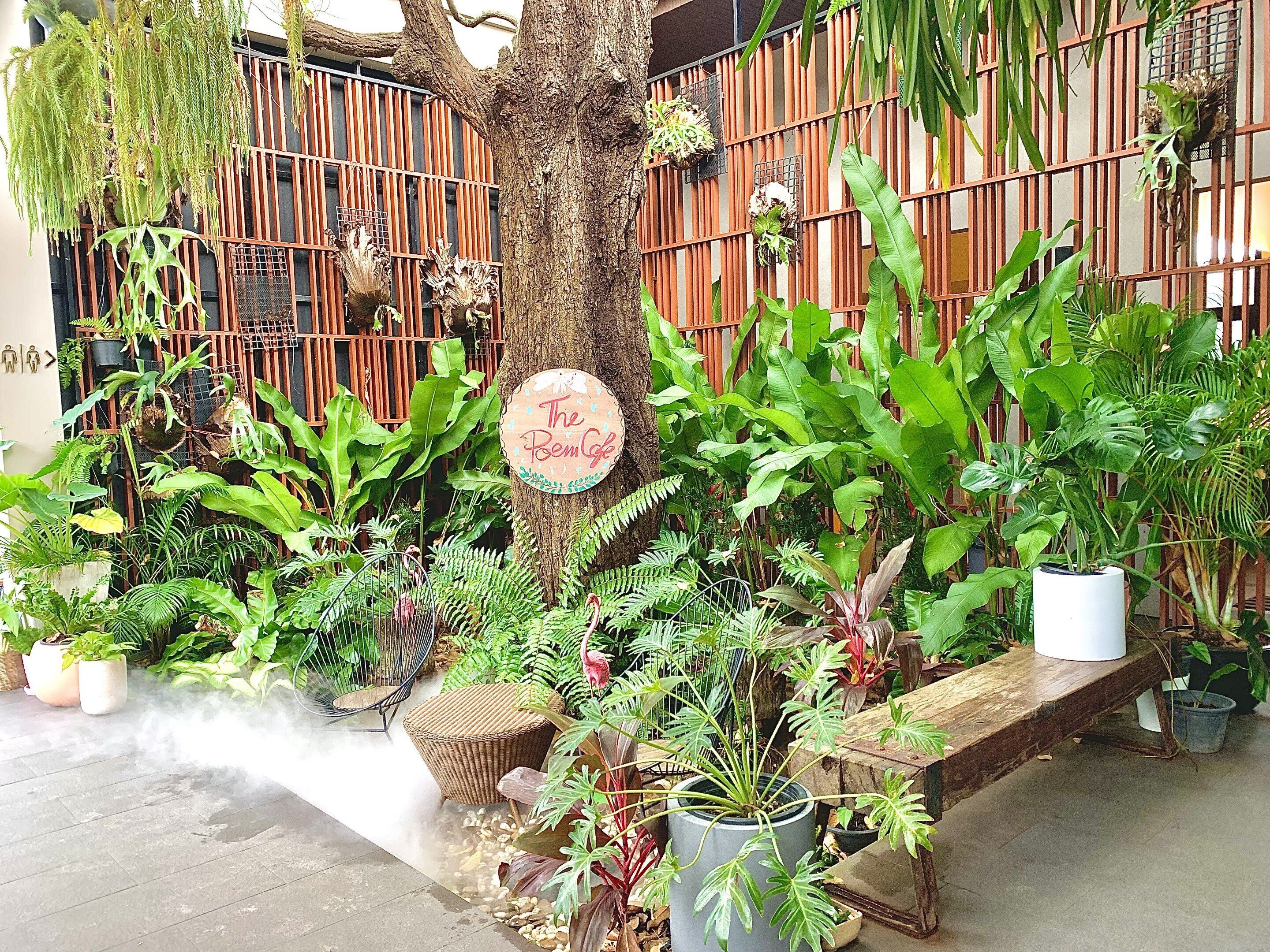 A lush garden area with a variety of potted plants and a sign that reads "The Poem Cafe."