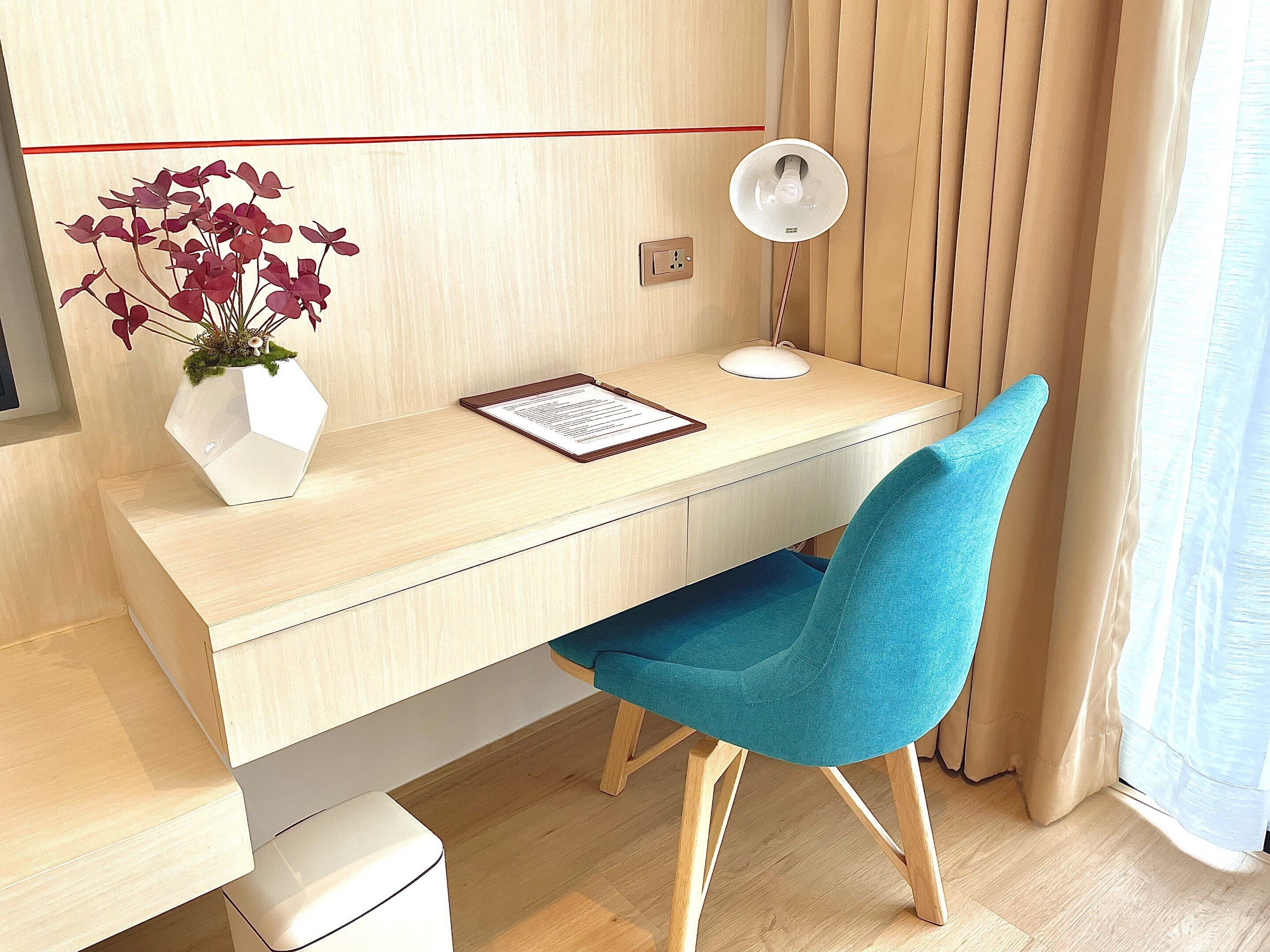 A modern desk with a white vase of flowers, a desk lamp, and a clipboard.