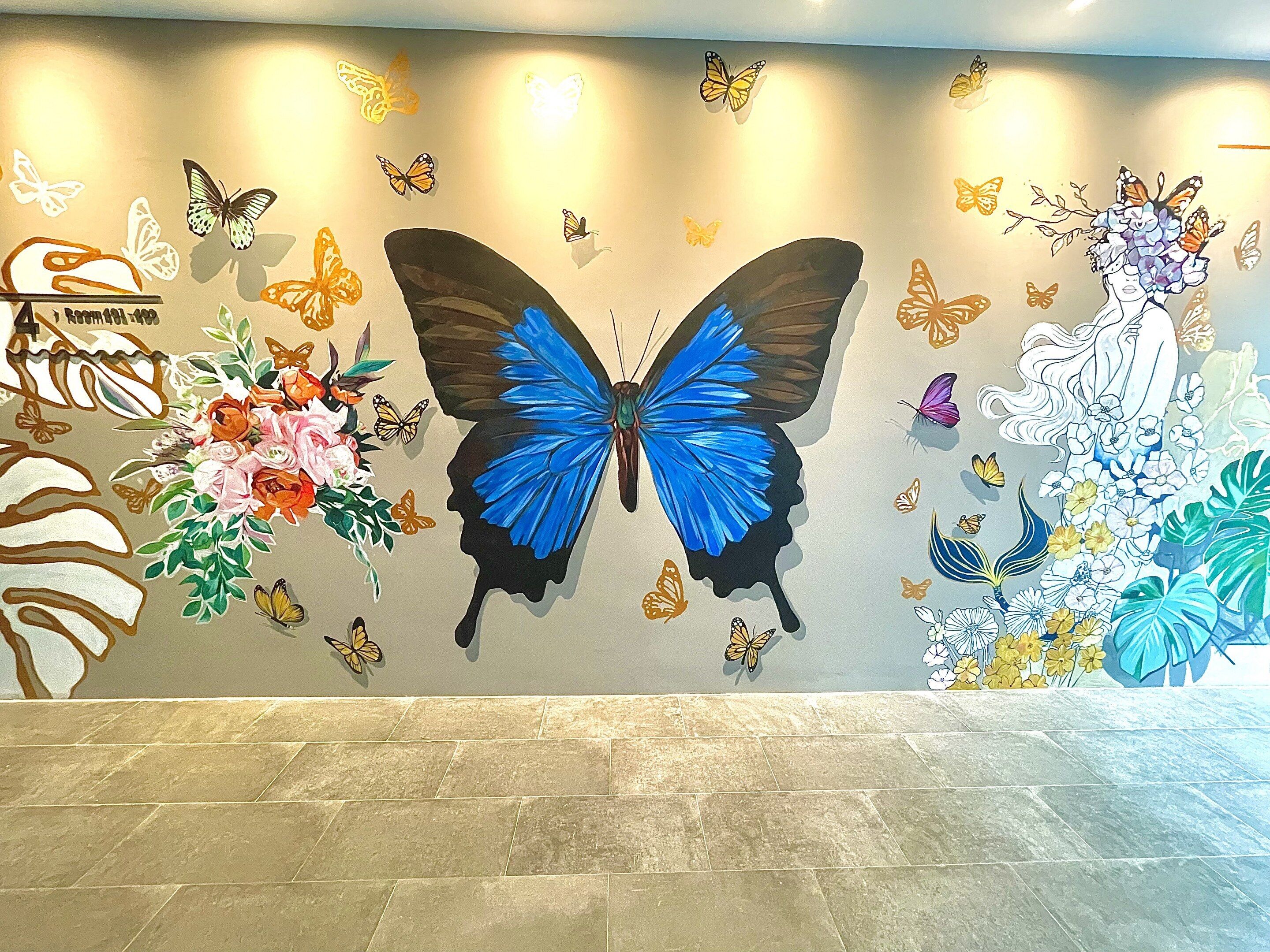 A wall with a large blue butterfly and various butterflies, flowers, and a woman with butterflies.