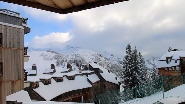 Un village de montagne enneigé, avec des bâtiments en bois et une voiture garée devant.