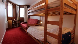 Une chambre avec un lit superposé, un tapis rouge, un bureau et une fenêtre avec des rideaux.