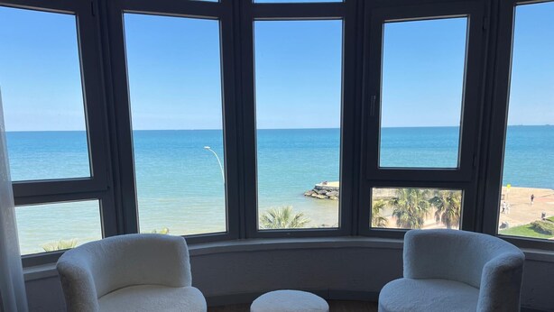 A room with a bay view, two white chairs, a small ottoman, and a red patterned rug. - New Hotel Samsun (Atakum)