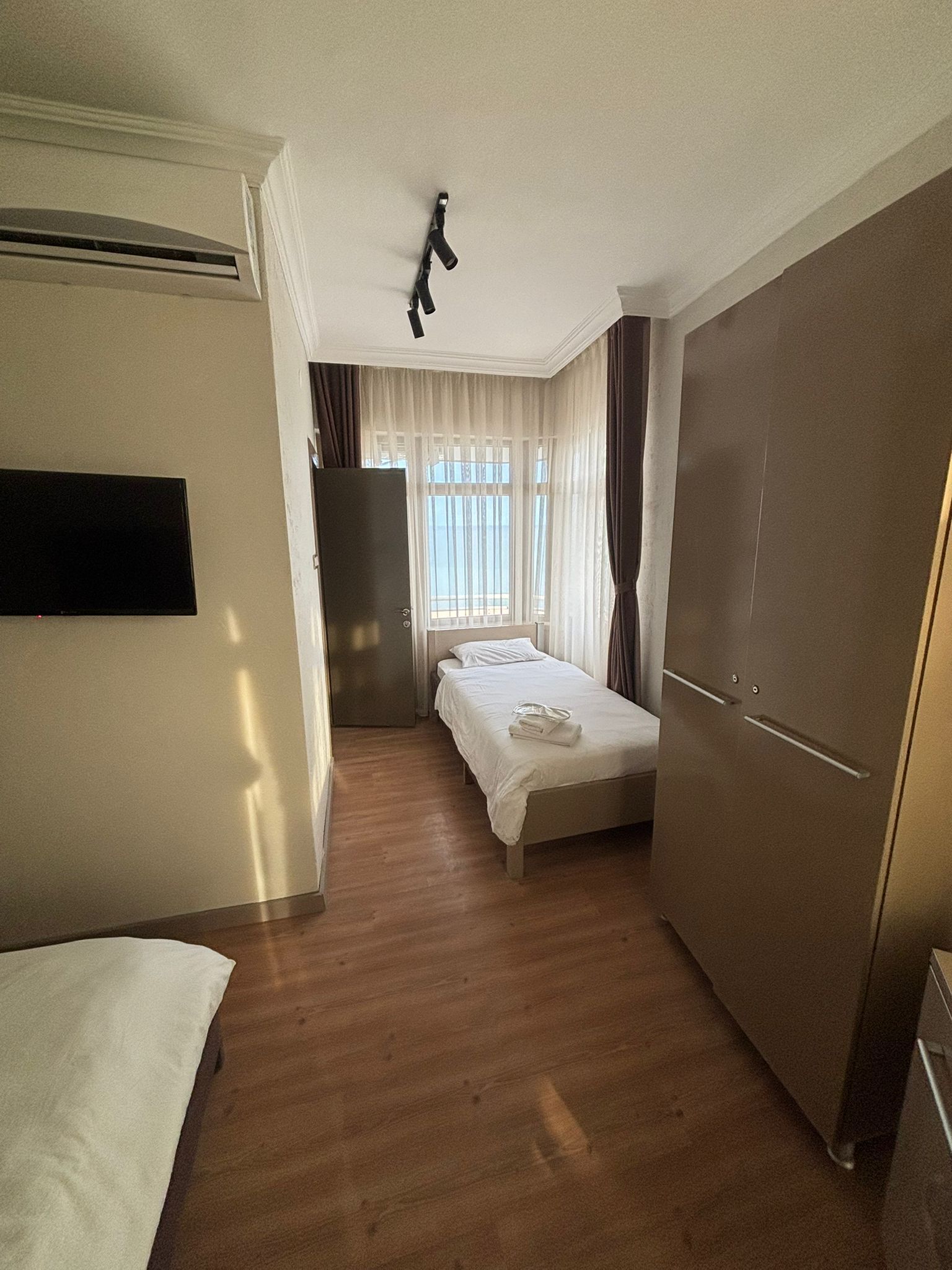 A hotel room with a bed, a wardrobe, a desk, and a window with curtains.