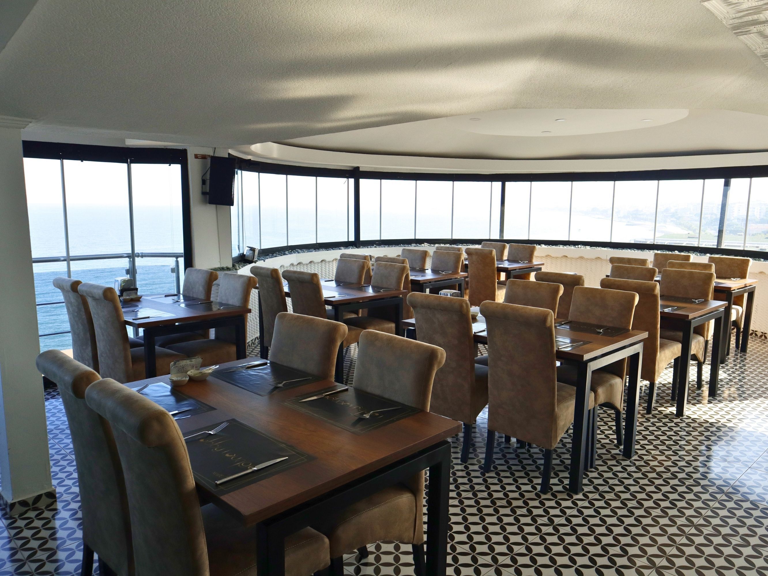 A dining area with tables and chairs, large windows, and a view of the sea.