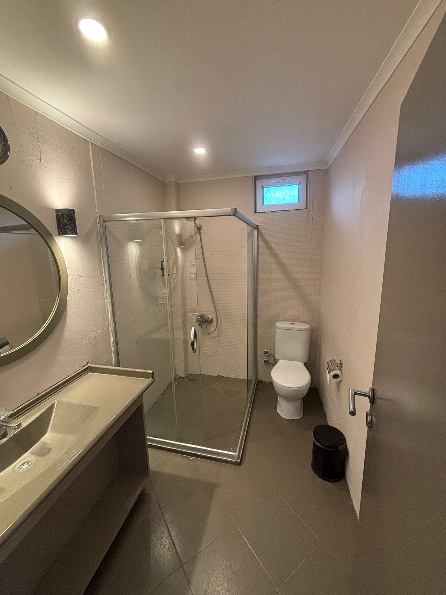 Un baño moderno con ducha envuelta en cristal, inodoro y lavamanos con espejo.