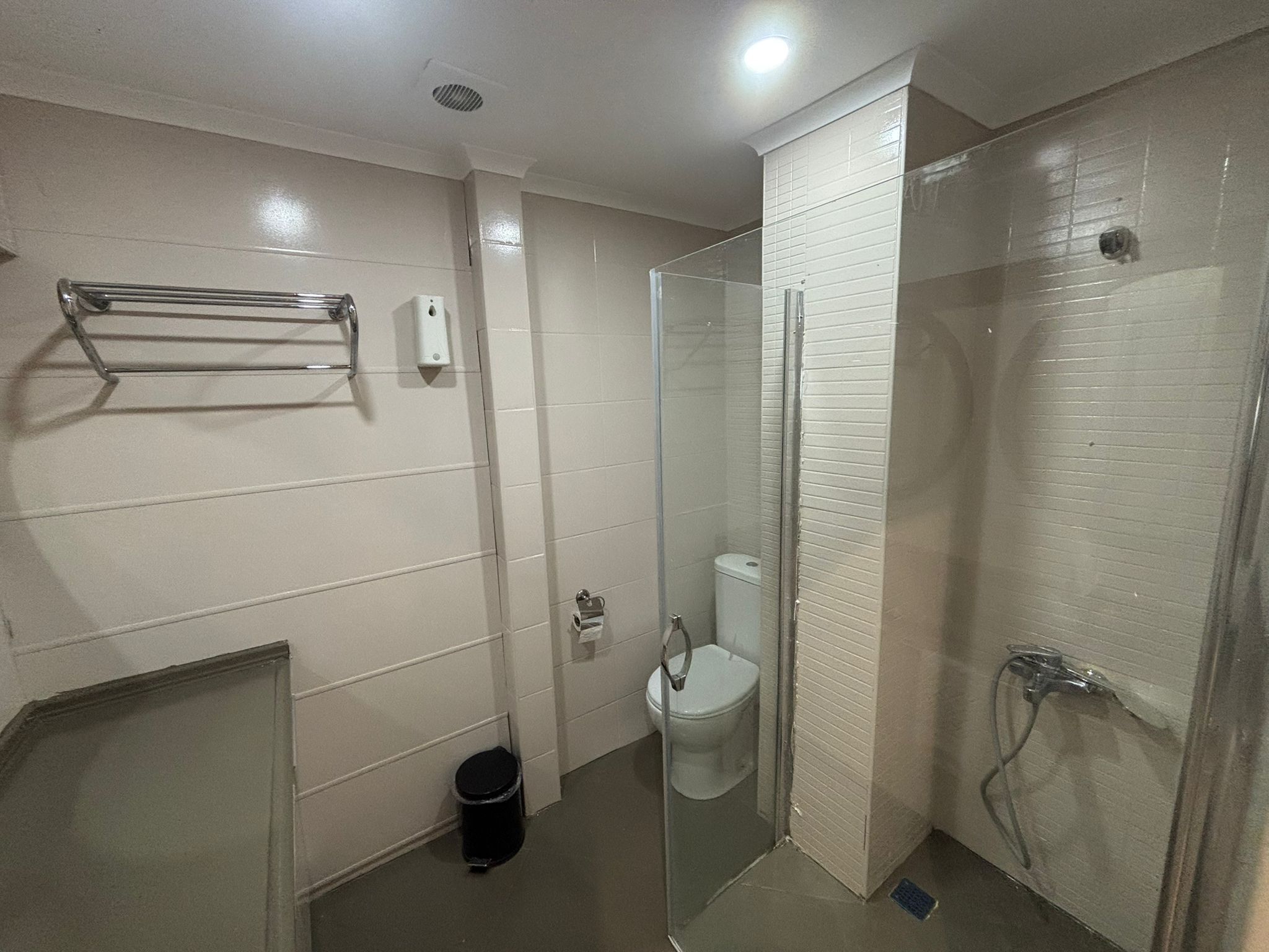 Un baño moderno con ducha envuelta en vidrio, inodoro y cubo de basura.