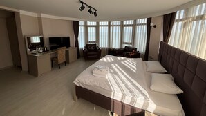 A modern hotel room with a large bed, a desk with a TV, and a view of the sea through large windows. - New Hotel Samsun (Atakum)
