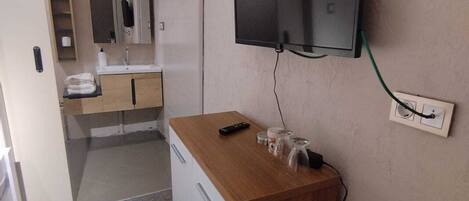 A compact hotel room with a kitchenette, a flat-screen TV mounted on the wall, and a small wooden table.