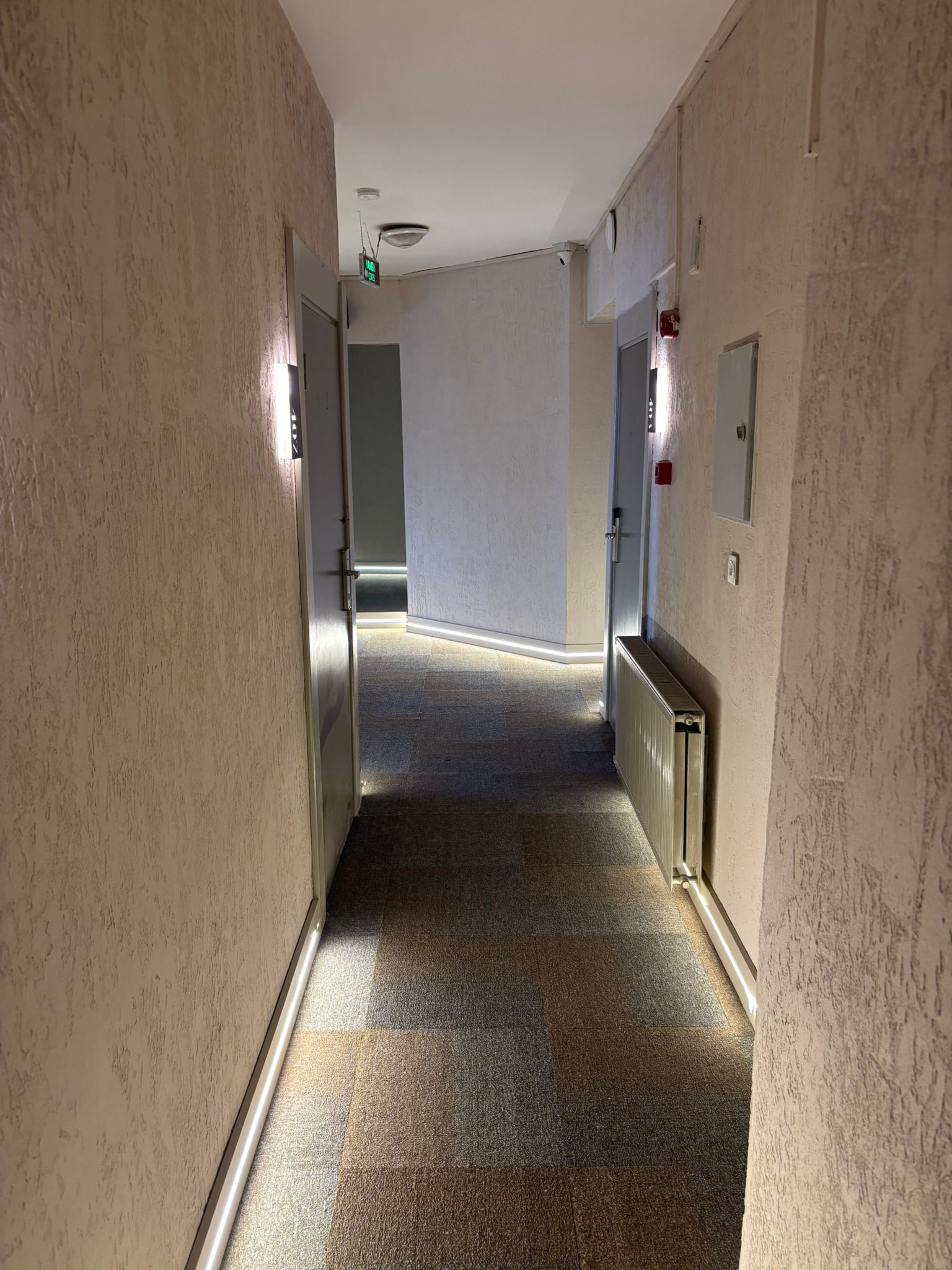 A hallway with beige textured walls, a tiled floor, and a door at the end.