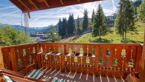 Une terrasse en bois offrant une vue sur un paysage montagneux, avec des arbres et un village situé au loin.