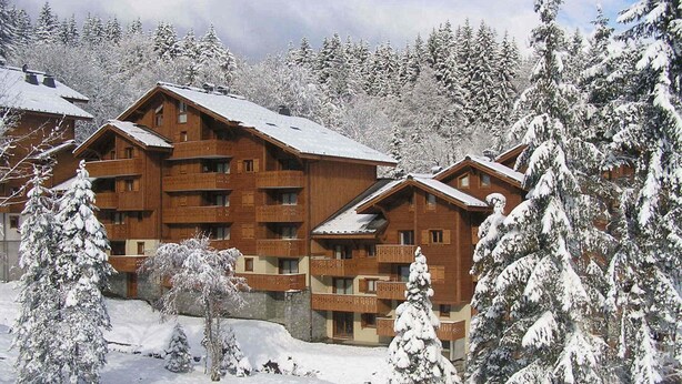 Un chalet en bois doté de plusieurs balcons, entouré d’arbres couverts de neige.