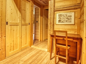 A wooden interior with a desk and chair, a framed picture on the wall, and wooden doors.