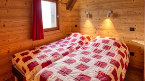 A wooden cabin bedroom with a bed, a window with red curtains, and two wall-mounted lights. - Chalet on the slopes with sauna and terrace, sleeps 12 (Morillon 1100)