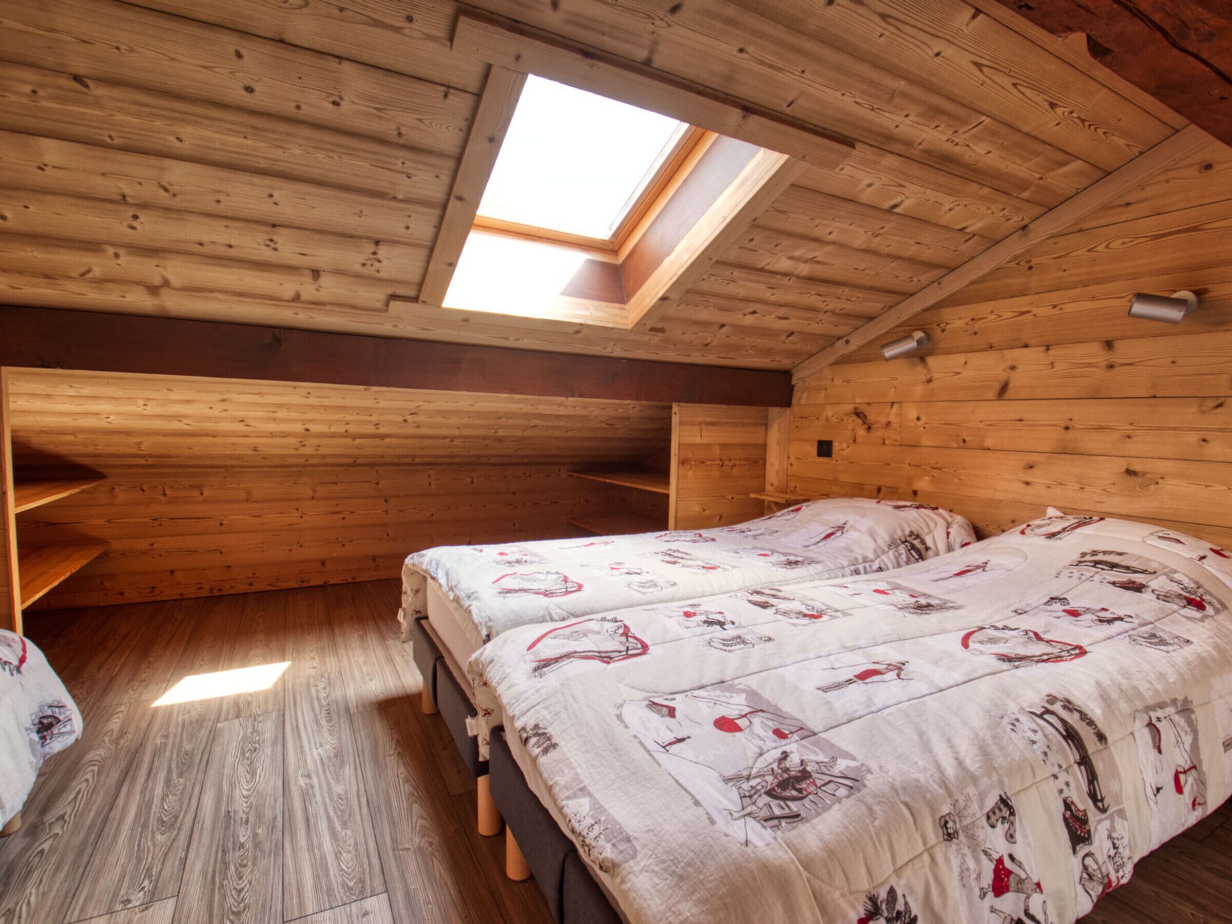 A cabin with two beds, a skylight, wooden walls, and a sloped ceiling.