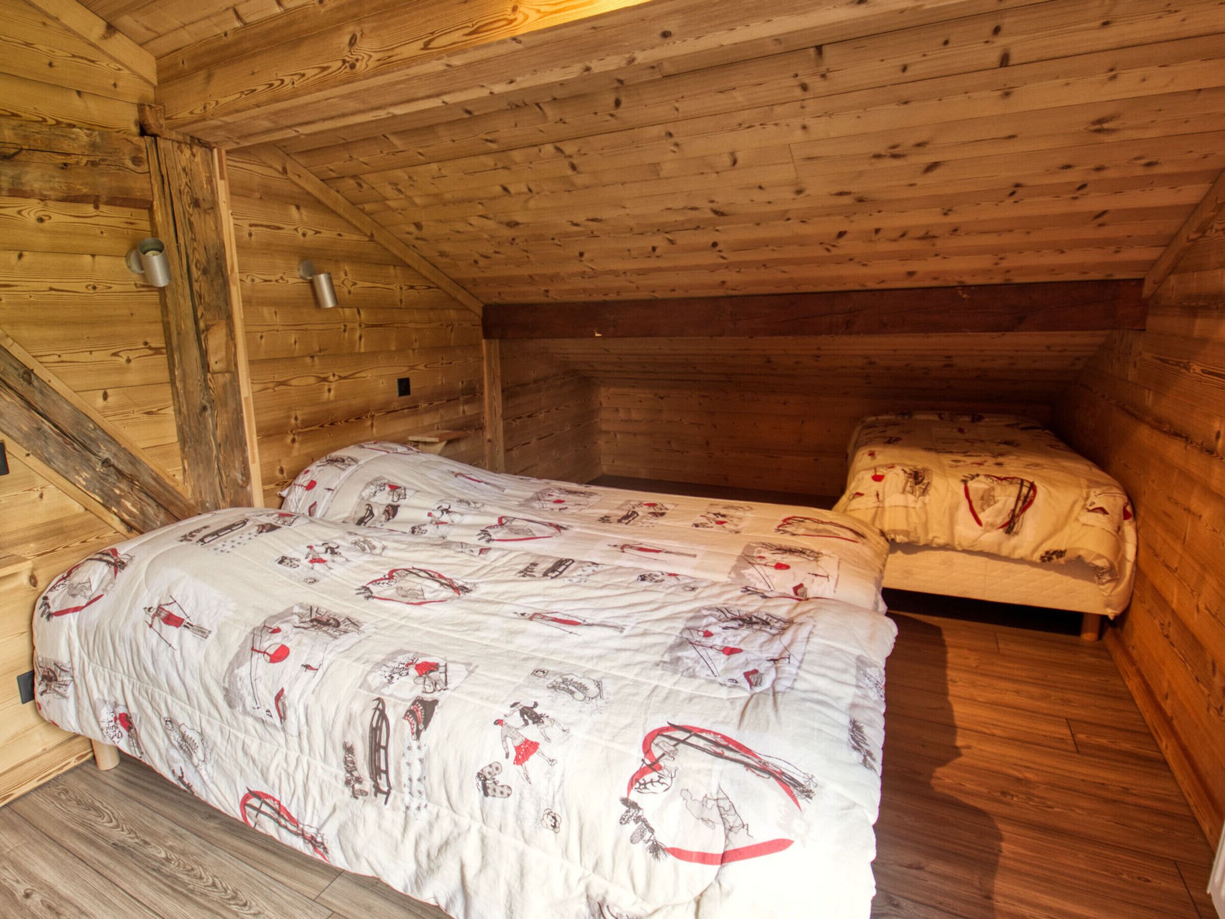 A cozy attic bedroom with a wooden ceiling and walls, a bed with a patterned duvet, and a small bench.