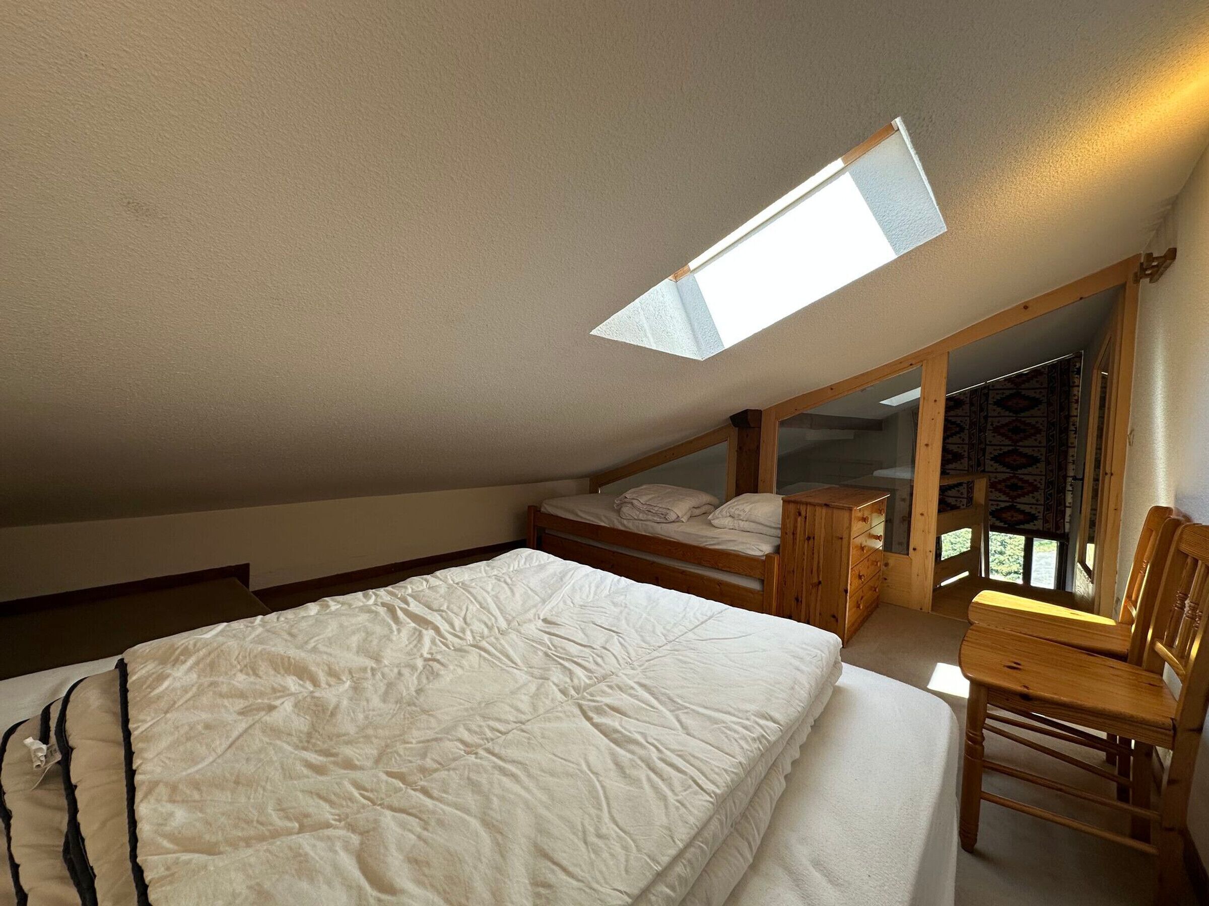 A bedroom with a skylight, a bed, a wooden nightstand, and a chair.
