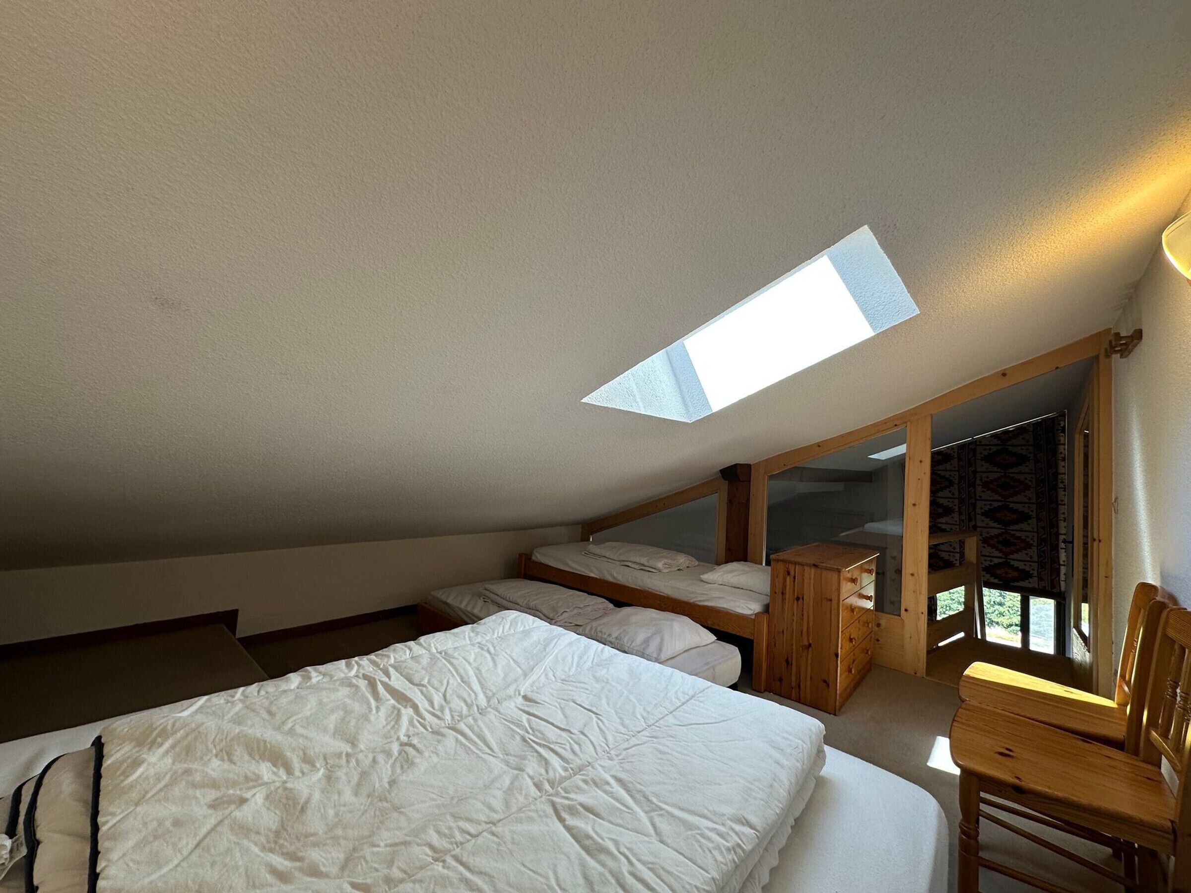 A bedroom with a skylight, two beds, a wooden dresser, and a chair.
