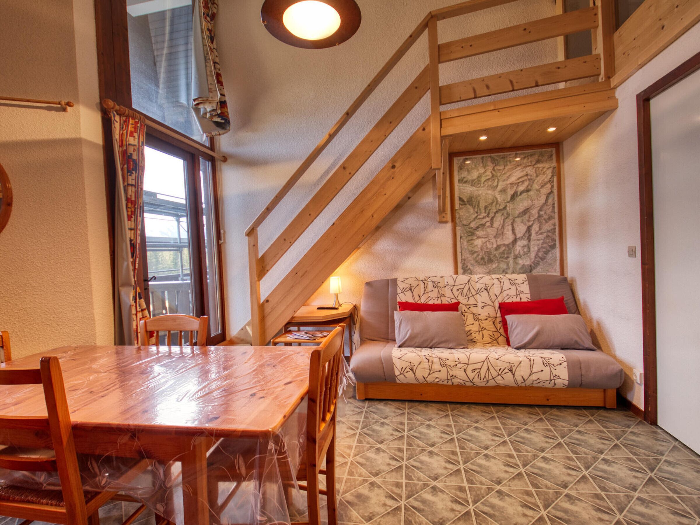 A cozy room with a wooden dining table, a sofa with patterned cushions, and a staircase leading to an upper level.