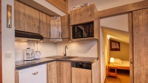 A compact kitchen with wooden cabinets, a Bosch dishwasher, a coffee maker, and a microwave. - Cozy mezzanine apartment in Morillon 1100 (Morillon 1100)