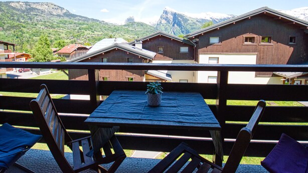A balcony with a table and chairs, overlooking a mountain landscape with houses. - Charming Duplex Mezzanine in Morillon Village (Morillon Village)