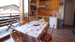 A rustic kitchen with wooden cabinets, a dining table with a patterned tablecloth, and a view of a building outside. - Charming Duplex Mezzanine in Morillon Village (Morillon Village)
