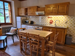 A kitchen with wooden cabinets, a microwave, a sink, and a dining area with a table and chairs. - Family-friendly townhouse with 2 apartments - ideal for large families (Morillon Village)