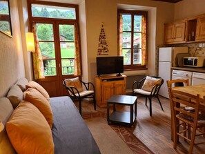 A cozy living room with a sofa, chairs, a TV, and a kitchen area with a microwave and refrigerator.