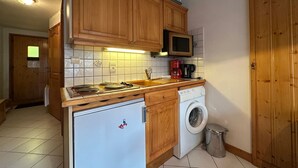 Een compacte keuken met houten kastjes, een magnetron, een kookplaat, een spoelbak en een wasmachine.