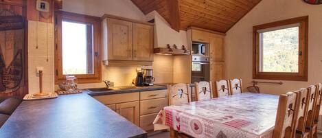 Una cocina con armarios de madera, una mesa de comedor con sillas y un reloj en la pared.