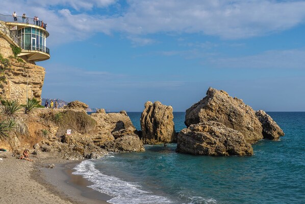 Un paysage côtier avec des formations rocheuses, une plage et un bâtiment doté d’un balcon donnant sur la mer.