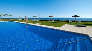A swimming pool with clear blue water, a grassy area with lounge chairs, and a view of the ocean. - 1 bedroom side sea view aparment (Torrox Costa)