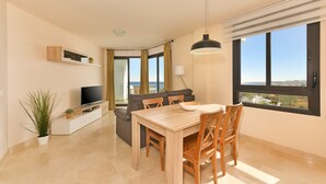 A modern living room with a dining area, a television, and a large window with a view. - 1 bedroom side sea view aparment (Torrox Costa)