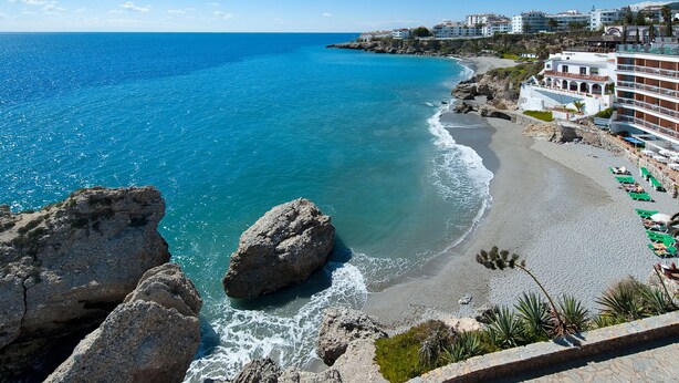 A coastal hotel with a beach view, rocky shoreline, and a row of sun loungers. - 1 bedroom side sea view aparment (Torrox Costa)
