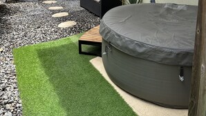Ein Garten mit Whirlpool, überdachtem Sitzbereich und kleinem Ziergarten mit Kunstgrün und trittfesten Steinen.