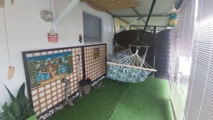 Ein Zimmer mit Strohdach, einer Hängematte, einem Gemälde und einem kleinen Fenster.