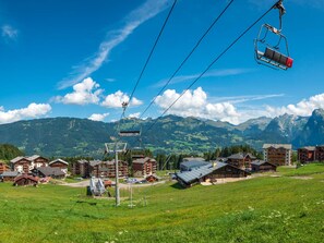 Un complejo turístico de montaña con telesilla, chalés y vistas a los Alpes.