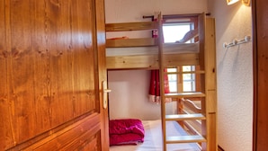 En køjeseng i træ med en stige, et vindue med gardiner og en lampe på væggen.