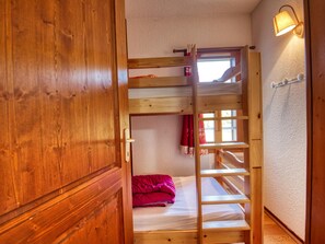 A wooden bunk bed with a ladder, a window with curtains, and a wall-mounted lamp.