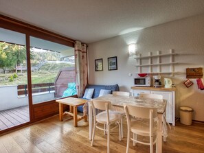 Une pièce chaleureuse avec une table à manger en bois, des chaises, un canapé et un coin cuisine équipé d’un four à micro-ondes et d’une bouilloire.
