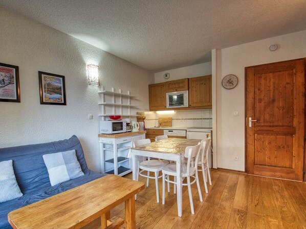 Un espace de vie compact comprenant un coin cuisine, une table à manger avec des chaises, un canapé et une porte en bois.