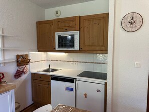 A compact kitchen with wooden cabinets, a built-in microwave, a sink, and a refrigerator. - Apartment for 4 people, near slopes and playground (Morillon 1100)