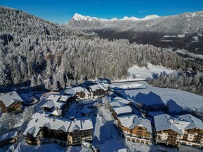 Une station de montagne enneigée, avec plusieurs bâtiments de style chalet, une piste de ski et une vallée boisée.