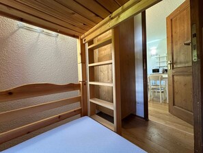 Un lit en bois avec une tête de lit, une étagère intégrée et une porte donnant sur un coin cuisine.