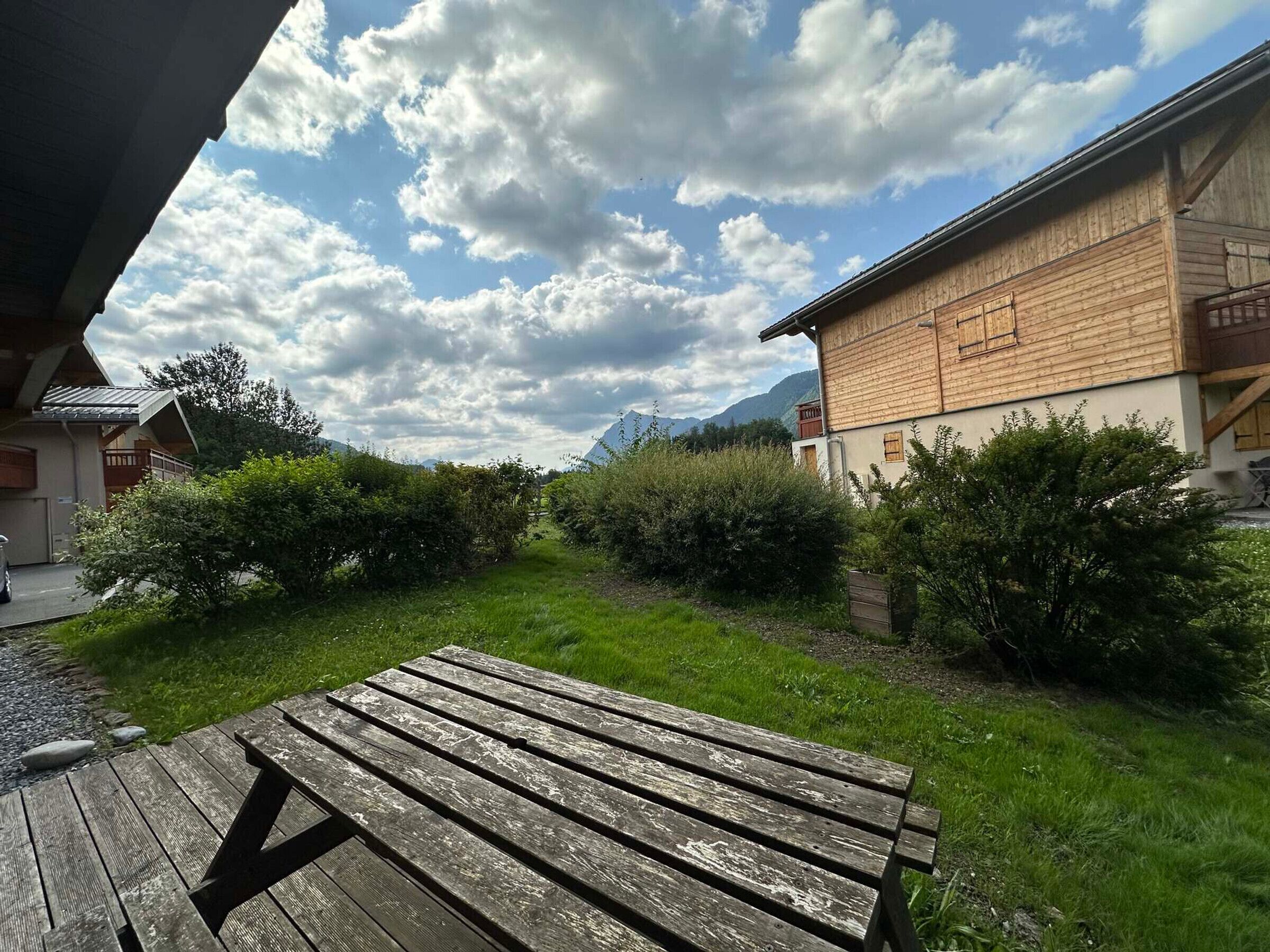 Ein rustikales Holzgebäude mit geneigtem Dach, umgeben von üppiger Vegetation und blauem Himmel.