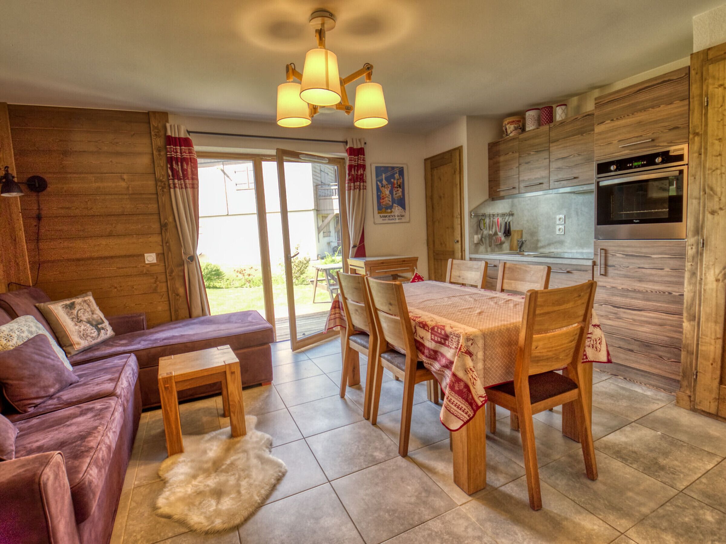 Un salon chaleureux avec un canapé, une table à manger et des chaises, une cuisine avec des meubles en bois et une porte-fenêtre coulissante donnant sur un jardin.