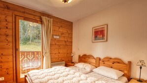 A wooden cabin bedroom with two beds, a window with curtains, a nightstand, and a painting on the wall.