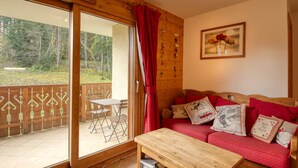 A cozy room with a wooden sofa, a wooden coffee table, and a sliding glass door leading to an outdoor area with a wooden deck and a table.