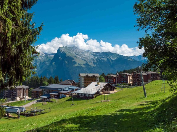 A mountain resort with buildings, a ski lift, and a view of snow-capped mountains.
