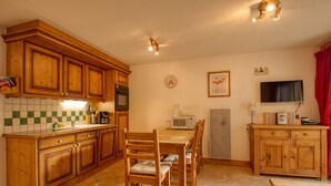 A kitchen with wooden cabinets, a dining table with chairs, a microwave, a coffee maker, and a television.
