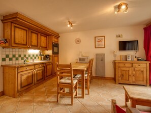 Une cuisine avec des meubles en bois, une table à manger avec des chaises, un four à micro-ondes, une machine à café et un téléviseur.